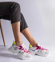 A person wearing vibrant sport sneakers with pink and yellow detailing, seated casually in black speckled pants.