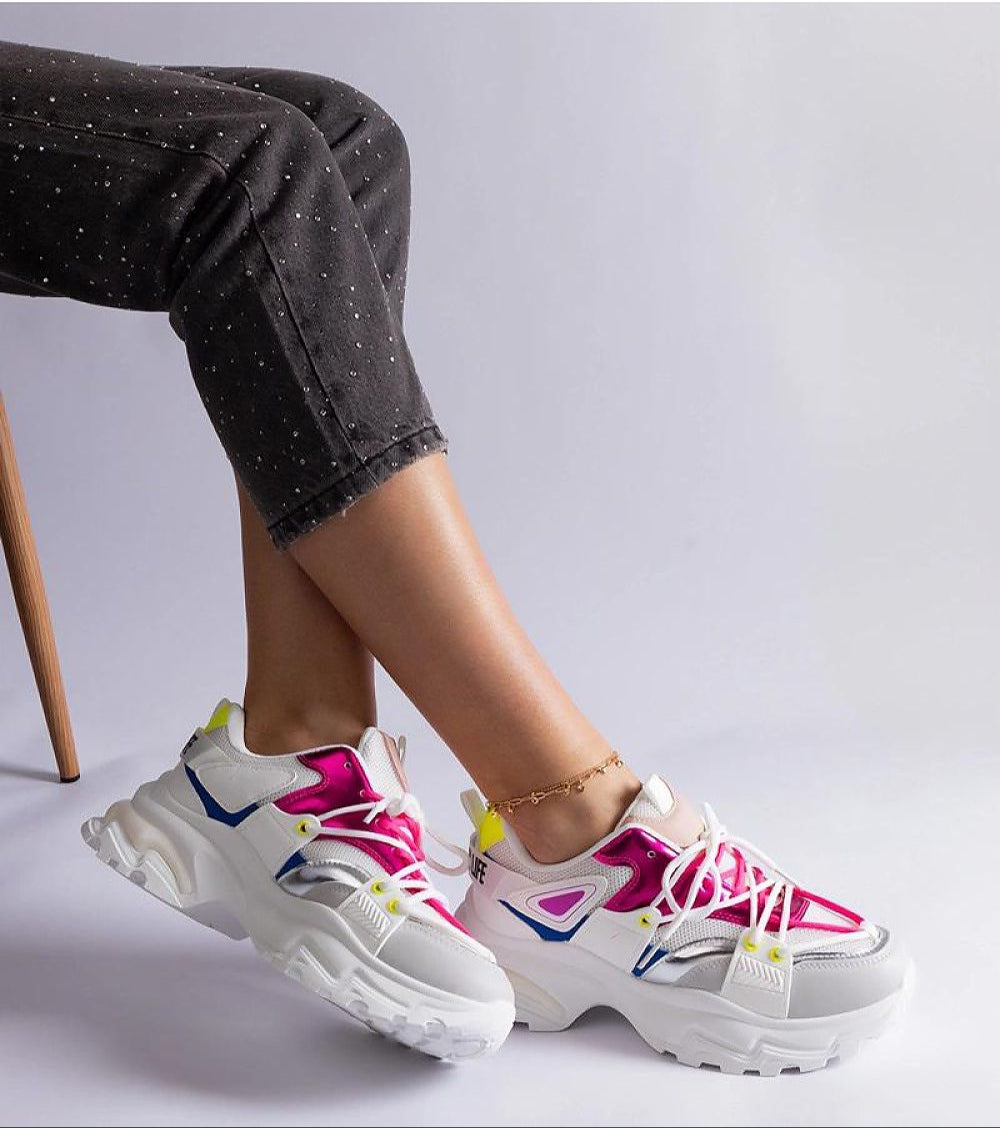 Woman wearing vibrant modern sneakers with pink and yellow accents, showcasing stylish footwear against a gray background.