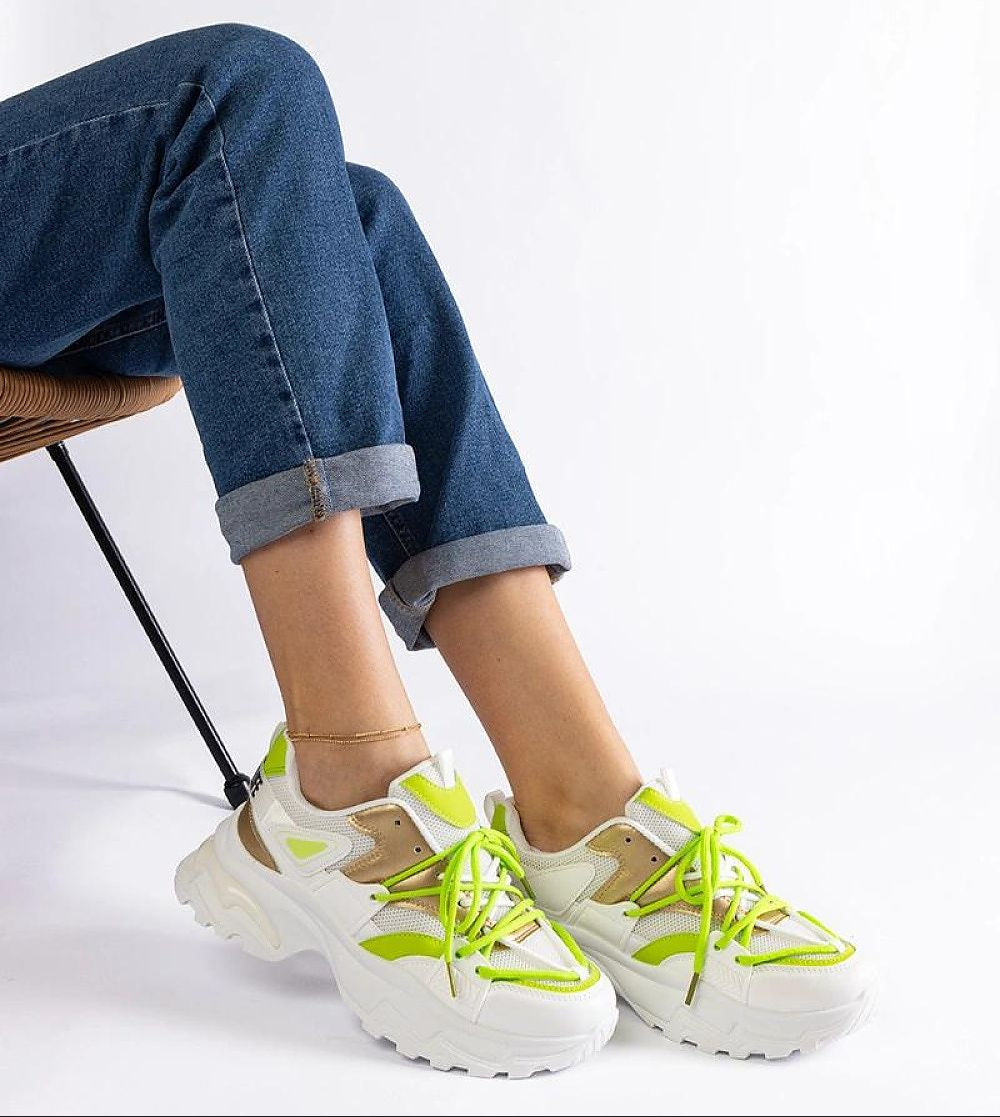Person wearing stylish neon green and white chunky sneakers with rolled-up jeans, sitting on a chair.