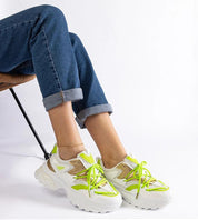 Person wearing stylish neon green and white chunky sneakers with rolled-up jeans, sitting on a chair.