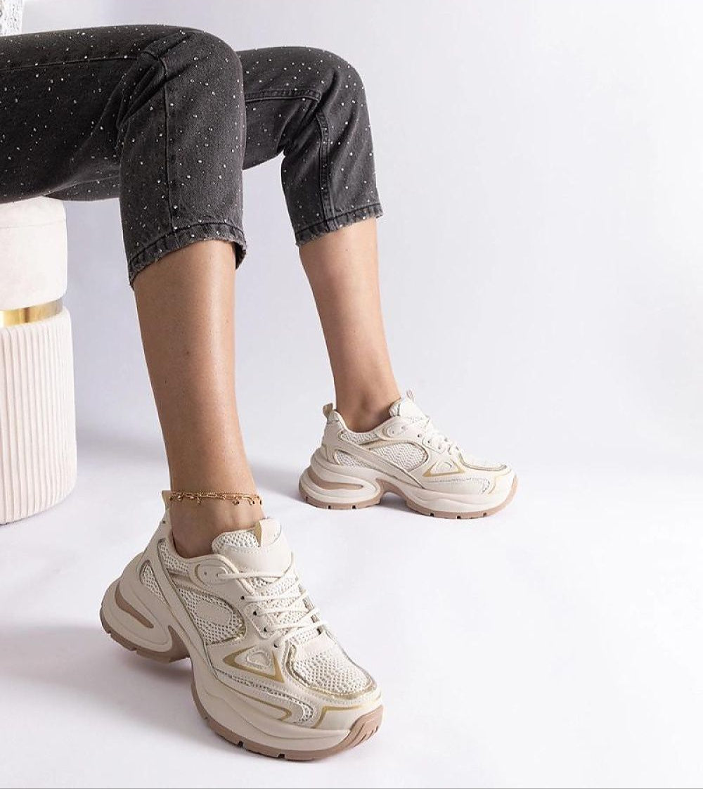 Woman wearing white chunky sneakers with thick sole, sitting in a stylish pose, showcasing modern casual fashion footwear.