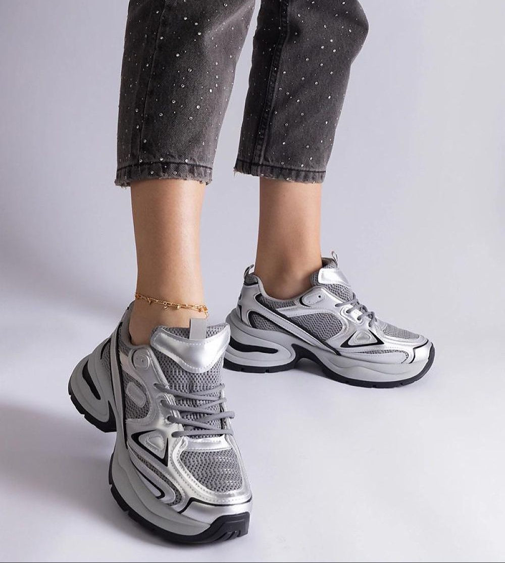 Silver metallic chunky sneakers with air mesh, worn with black ankle jeans, featuring multi-layer sole for a stylish urban look.