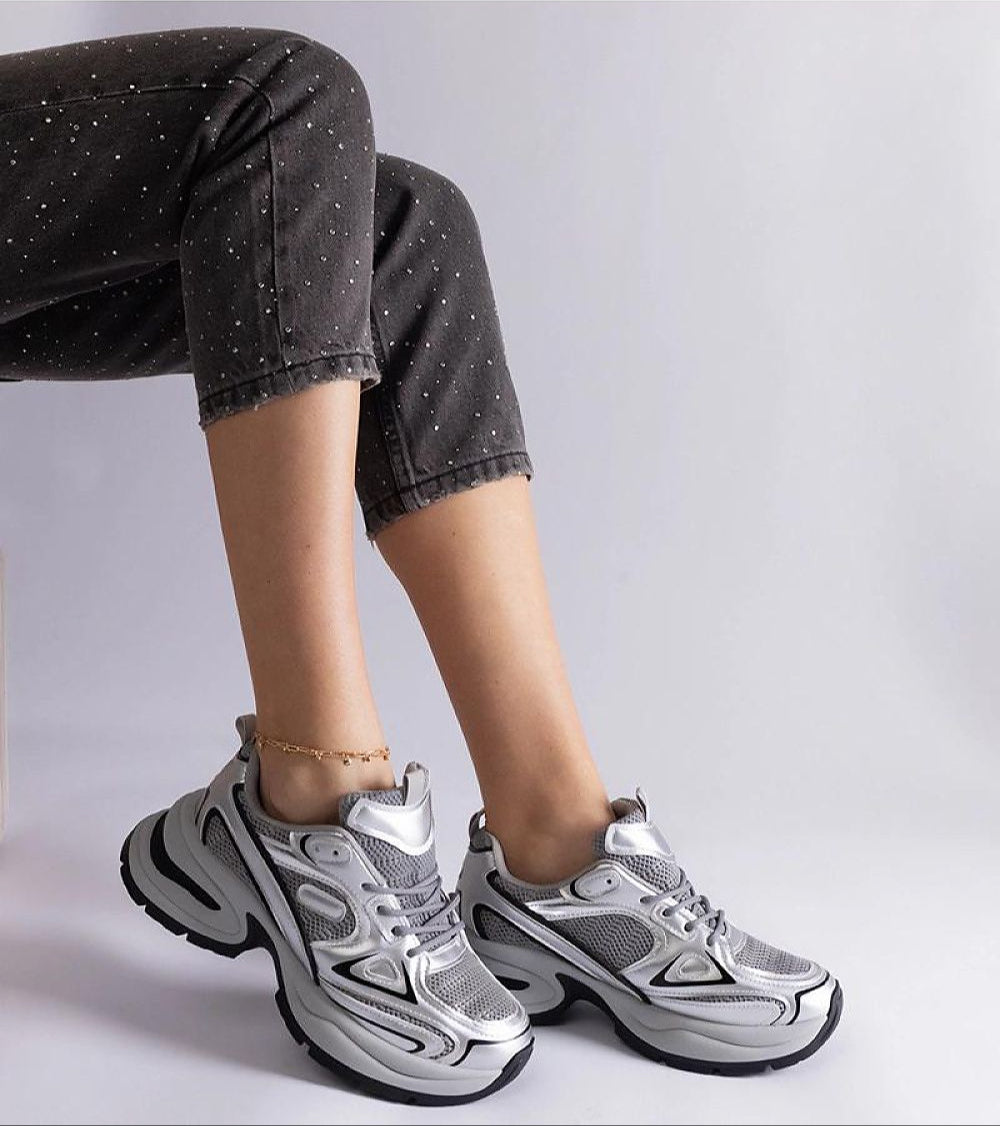 Person wearing silver chunky sole sneakers with black jeans, showcasing a stylish and modern footwear design.
