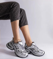 Person wearing silver chunky sole sneakers with black jeans, showcasing a stylish and modern footwear design.