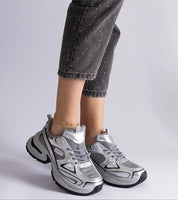 Woman wearing silver chunky sole sneakers paired with gray jeans, showcasing modern and stylish footwear design.