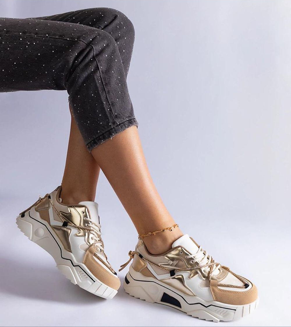 Stylish beige and white sneakers with gold accents worn with black jeans, showcasing a modern and trendy footwear design.