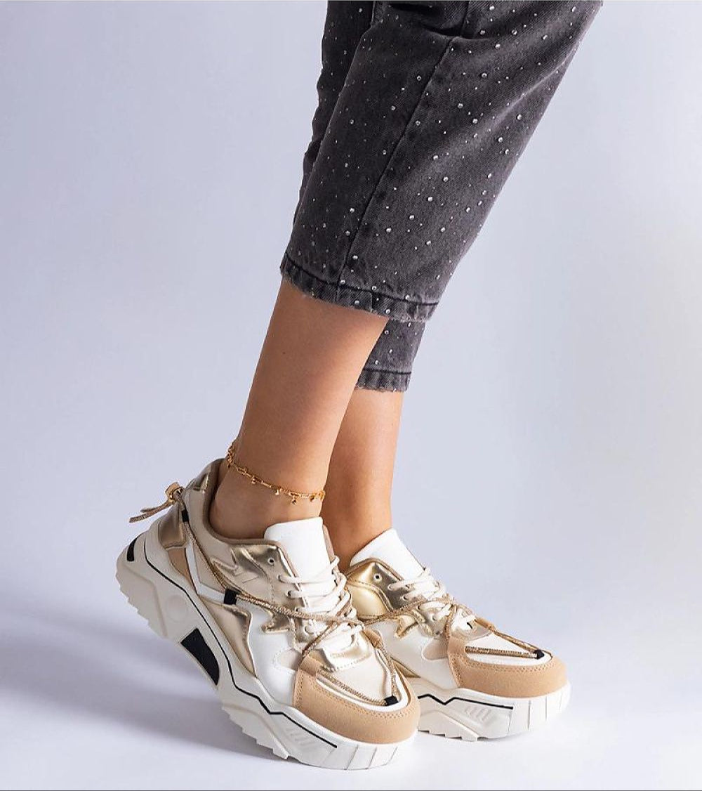 Woman wearing stylish beige and white chunky sneakers with gold accents, paired with cropped dotted pants.
