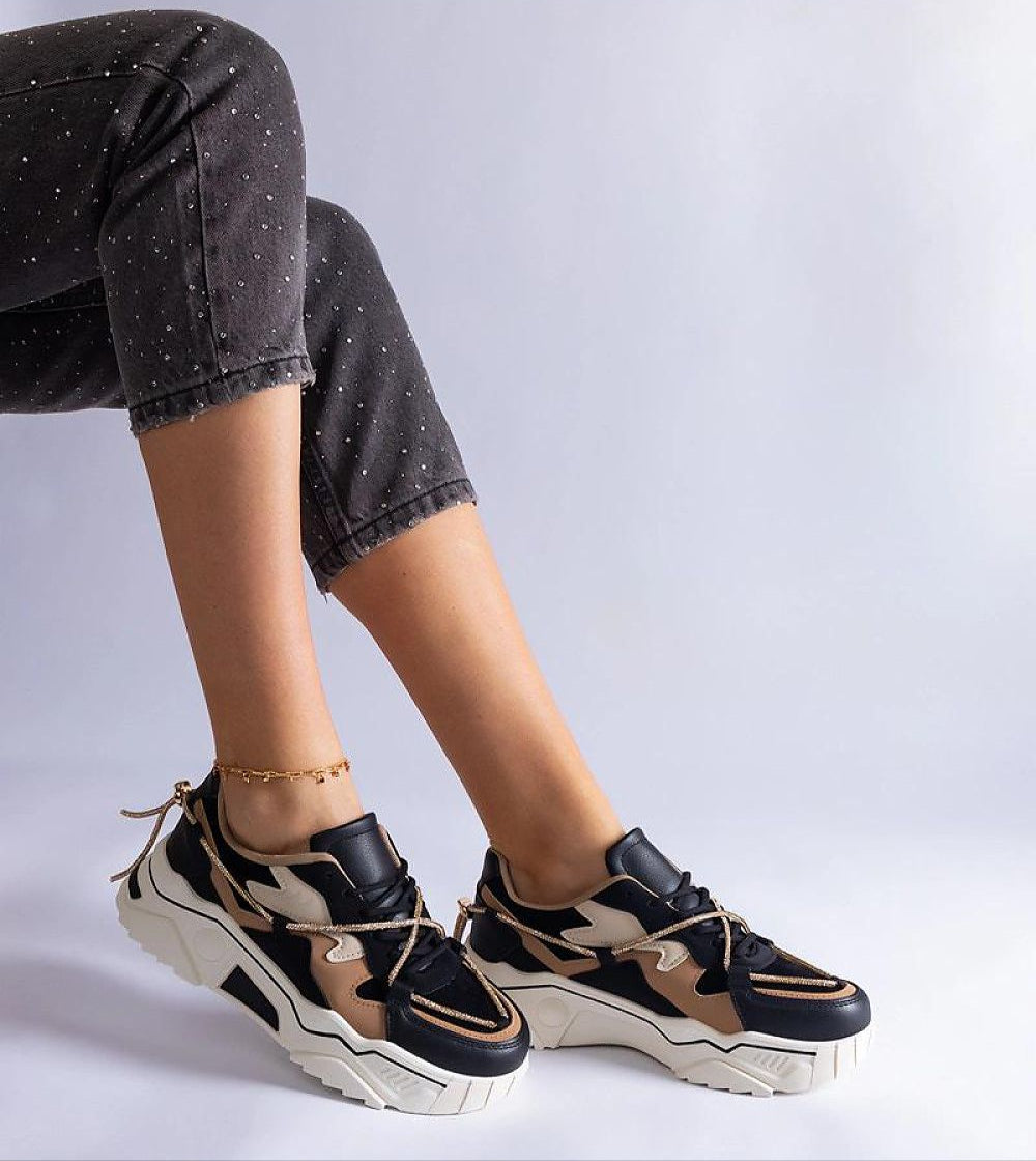 Stylish sneakers in black and tan with a chunky white sole on a person's feet, paired with black dotted jeans.