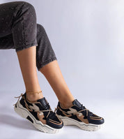 Stylish sneakers in black and tan with a chunky white sole on a person's feet, paired with black dotted jeans.
