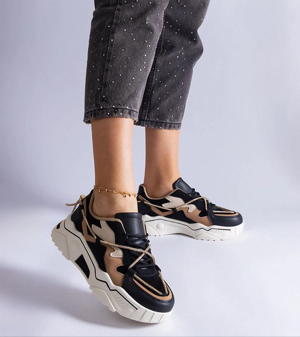 Woman wearing black and beige chunky sneakers with white soles, paired with dark jeans. Fashionable footwear for casual style.