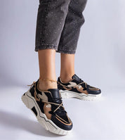 Woman wearing black and beige chunky sneakers with white soles, paired with dark jeans. Fashionable footwear for casual style.