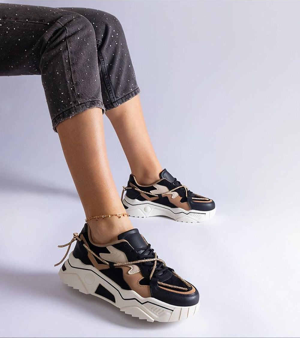 Person wearing trendy black and brown sneakers with chunky white soles, paired with dark dotted pants.