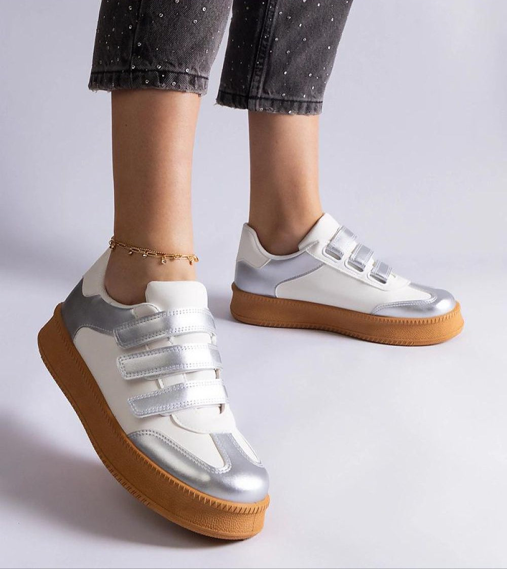Silver and white Velcro sneakers with brown rubber sole, worn with cropped pants and ankle bracelet, showcasing modern street style.
