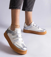 Silver and white Velcro sneakers with brown rubber sole, worn with cropped pants and ankle bracelet, showcasing modern street style.
