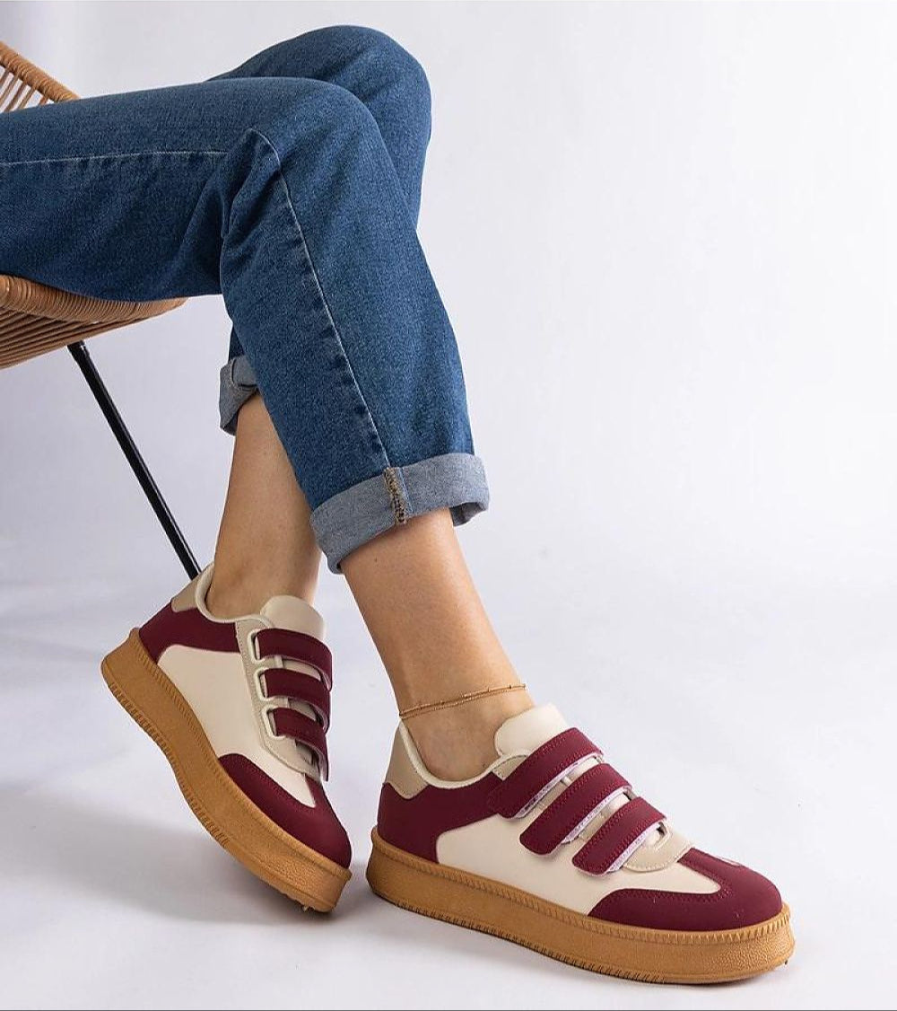 Person wearing stylish maroon and cream Velcro sneakers with a brown rubber sole, paired with rolled-up jeans for a casual look.