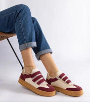 Person wearing red and white Velcro sneakers with brown soles and rolled up jeans, sitting on a chair.