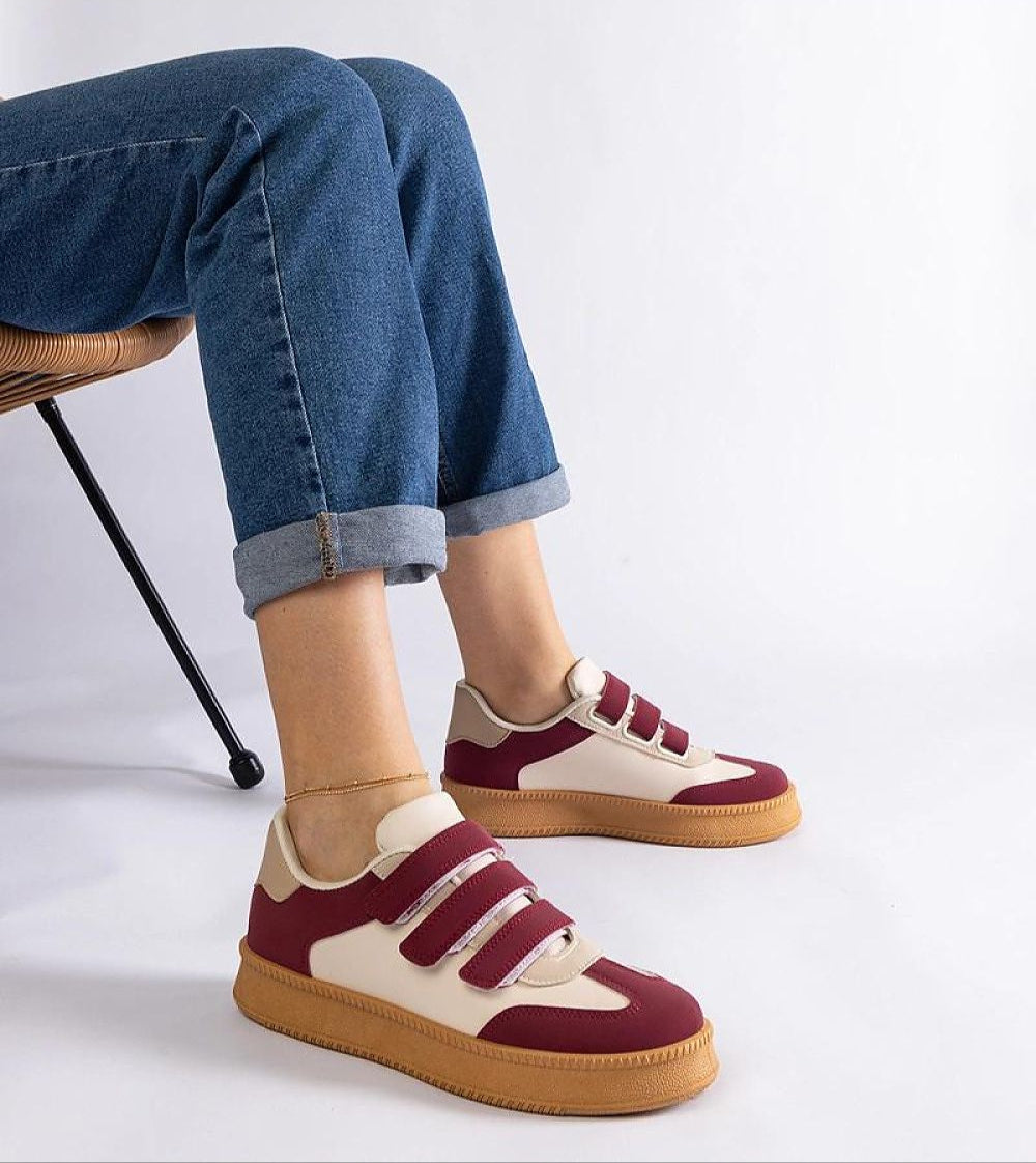 Person wearing maroon and white Velcro sneakers with gum soles, sitting on a chair in rolled-up jeans. Stylish and casual footwear.