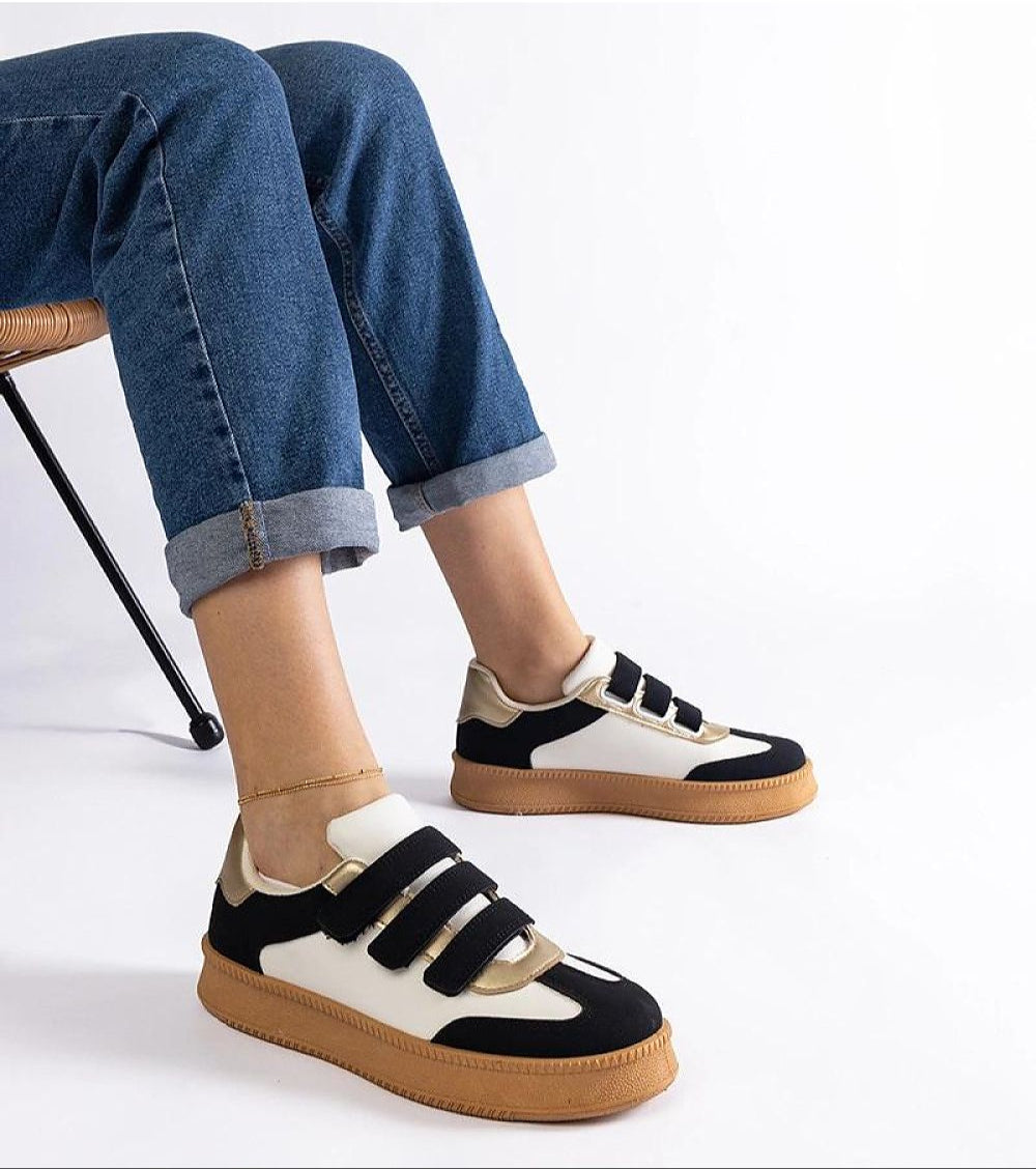Person wearing Elurea Gold Velcro Street Sneakers with a brown sole and eco leather design, paired with rolled jeans on a chair.