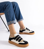Person wearing Elurea Gold Velcro Street Sneakers with a brown sole and eco leather design, paired with rolled jeans on a chair.