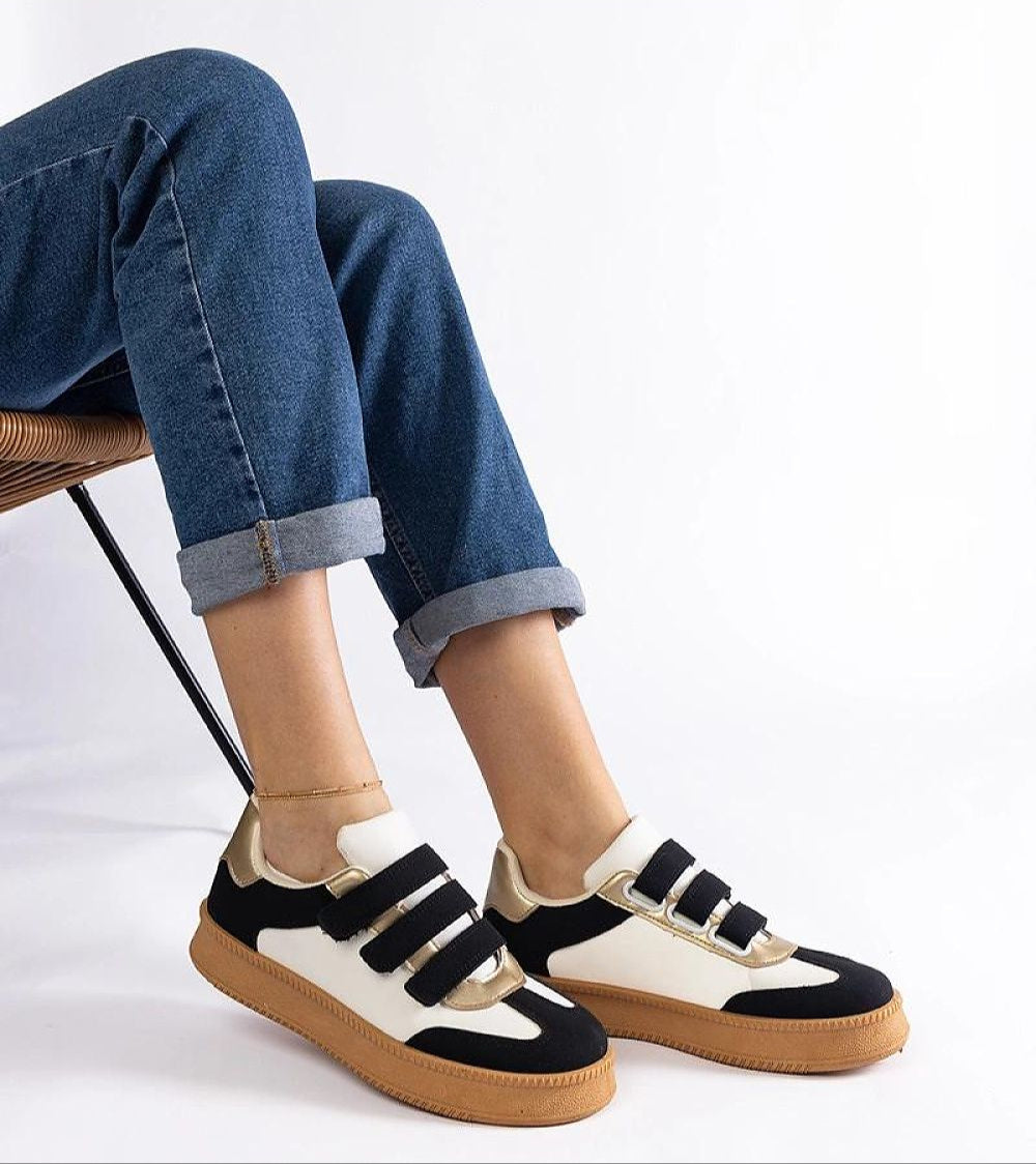 Person wearing Elurea Gold Velcro Street Sneakers with denim jeans, showcasing sleek eco leather design and brown rubber sole.