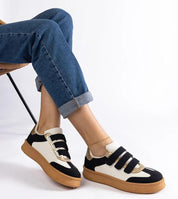 Person wearing Elurea Gold Velcro Street Sneakers with jeans, featuring golden sheen, eco leather, and brown rubber sole on a chair.