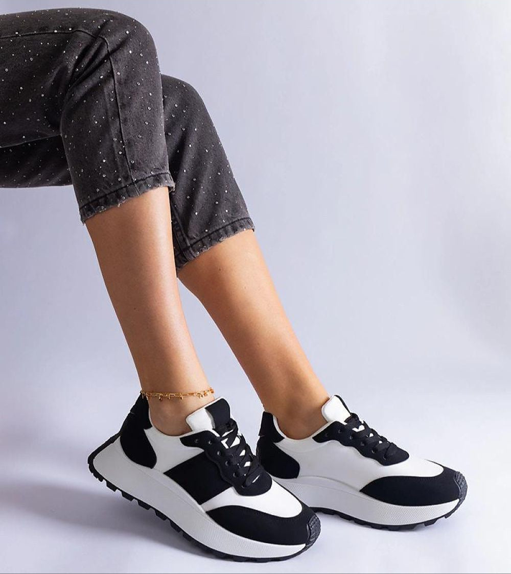 Person wearing black and white platform sneakers with gray polka dot pants, showcasing a trendy and minimalist style.