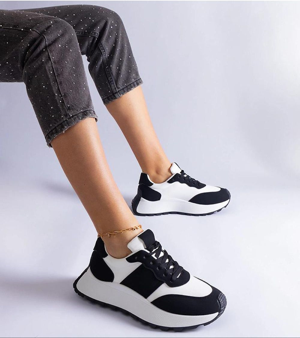 Person wearing black and white minimalist platform sneakers with cuffed pants, showcasing modern and versatile footwear style.