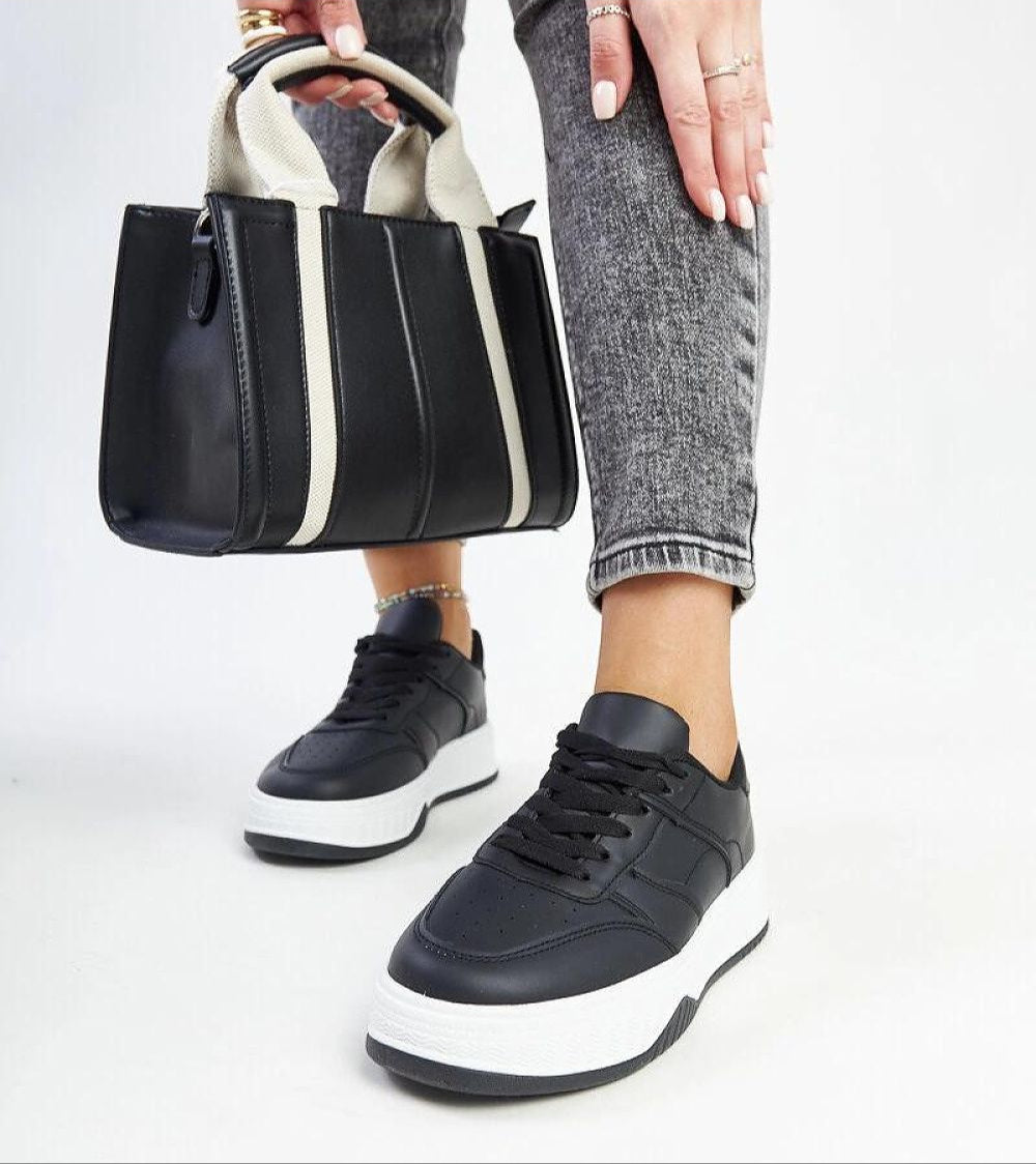 Woman wearing Kaedira Bold Platform Sneakers with a black and white handbag, showcasing high-platform style and modern fashion.