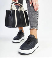 Woman wearing Kaedira Bold Platform Sneakers with a black and white handbag, showcasing high-platform style and modern fashion.