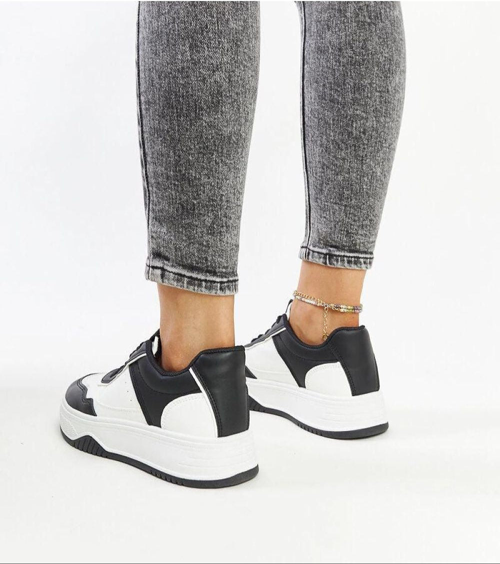 Vartema platform sneakers in black and white, eco suede leather, with chunky sole, worn on a person with grey jeans. Fashionable footwear.