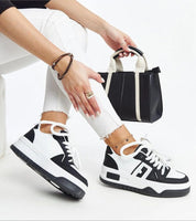 Person wearing Noira platform sneakers in black and white, paired with white jeans and holding a stylish black handbag.