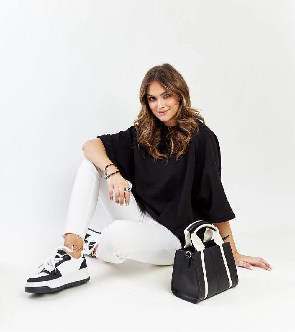 Woman wearing Noira platform sneakers with black-and-white design, seated in casual outfit, black handbag beside her.
