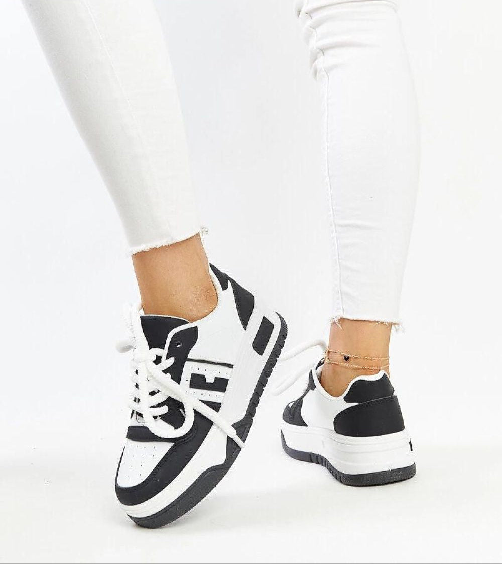 Person wearing Noira platform sneakers in black and white eco-leather with thick soles, paired with white jeans.