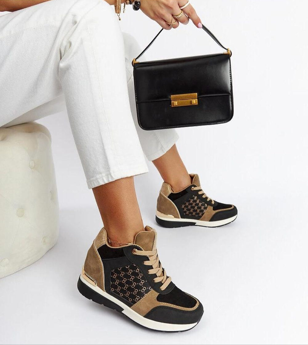 Fashionable woman wearing Lazetta black wedge sneakers with stylish black handbag and white pants.