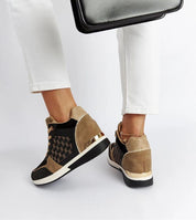 Woman wearing Lazetta black wedge sneakers with eco-leather and gold accents, paired with white pants, showing side and back view.