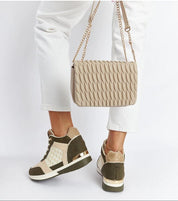 Fashionable wedge sneakers paired with white pants and a stylish quilted beige handbag, showcasing modern casual elegance.