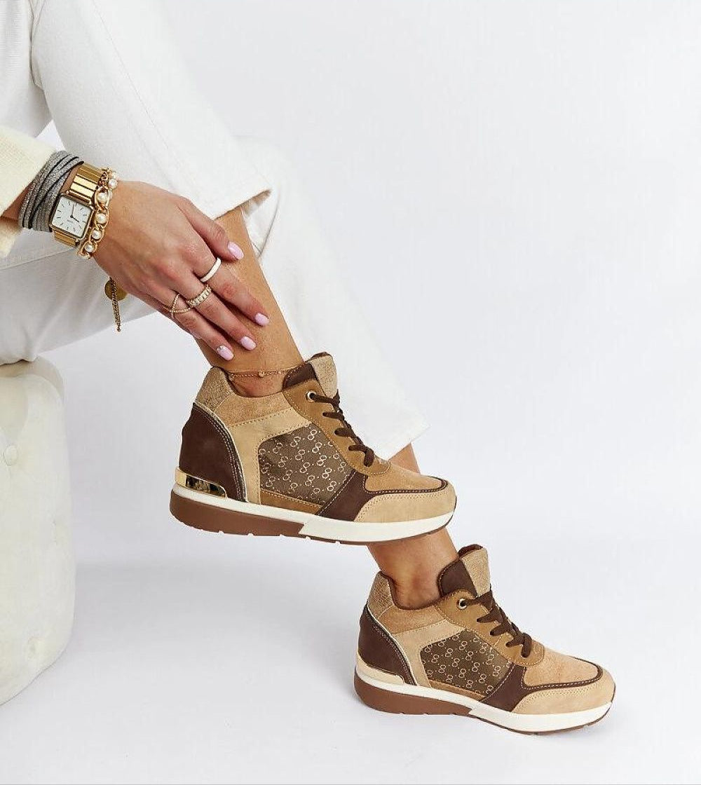 Person wearing stylish brown suede sneakers with white laces, light pants, and a watch. Footwear is complemented by assorted bracelets.