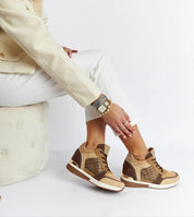 Woman wearing stylish brown wedge sneakers with white pants and a beige jacket, showcasing casual elegance and comfort.