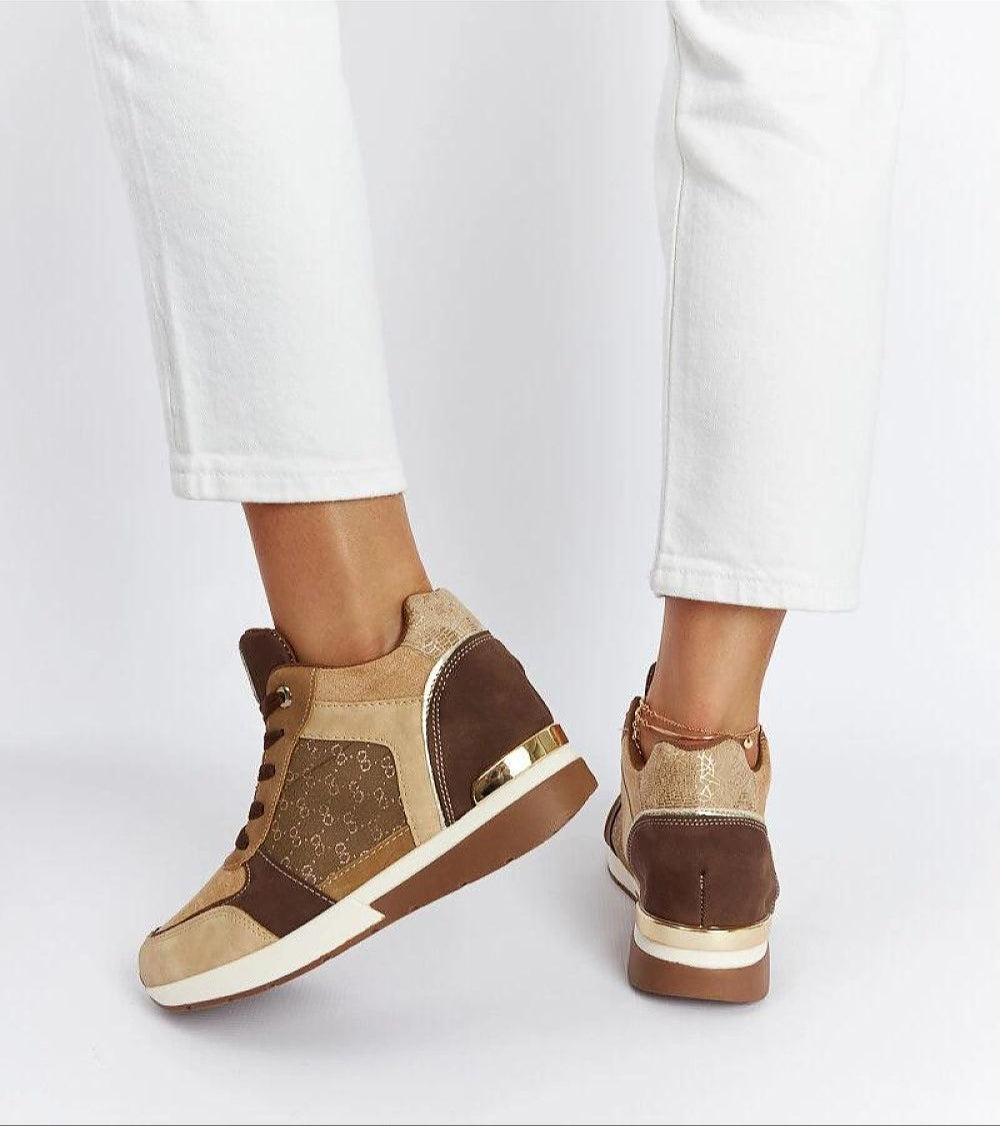 Person wearing brown wedge sneakers with gold accents and white pants, demonstrating style and comfort.
