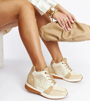 Stylish beige wedge sneakers paired with a matching clutch, worn by a seated woman in chic fashion.