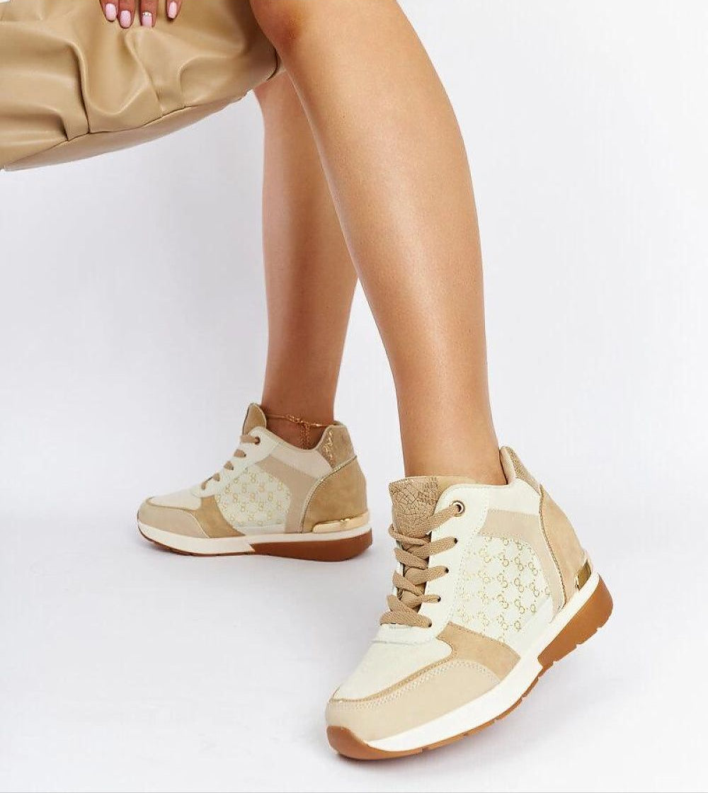 Stylish beige wedge sneakers with lace-up design and perforated details, paired with a tan handbag, worn by a woman seated.