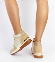 Person wearing beige and white wedge sneakers with gold trim, showcasing back view and ankle details on a white background.