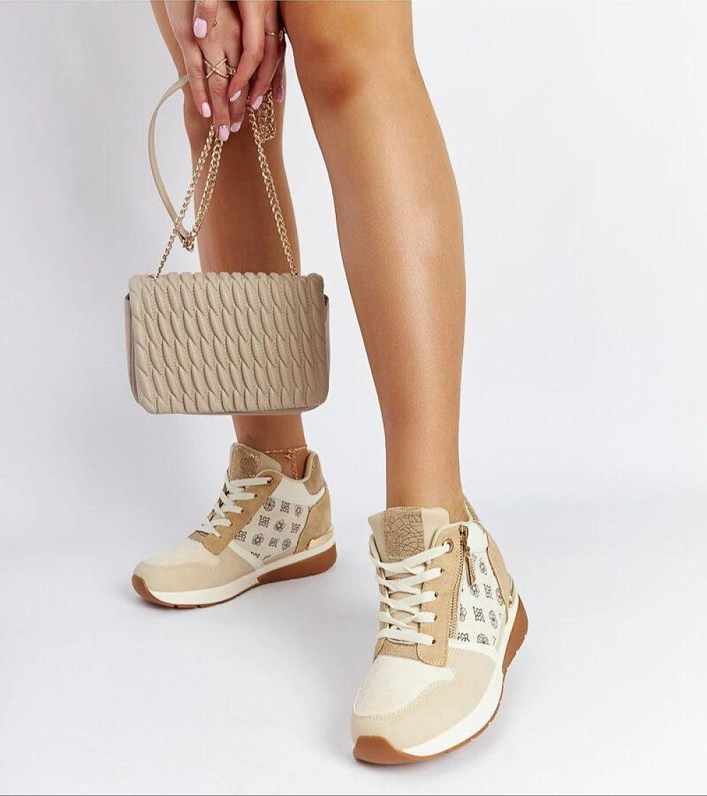 Stylish woman wearing beige sneakers with wedge heel, holding a tan quilted handbag, showcasing trendy casual footwear