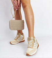 Stylish woman wearing beige sneakers with wedge heel, holding a tan quilted handbag, showcasing trendy casual footwear