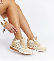 Stylish high-top beige sneakers with lace-up closure paired with gold bracelets, showcasing a chic casual look.