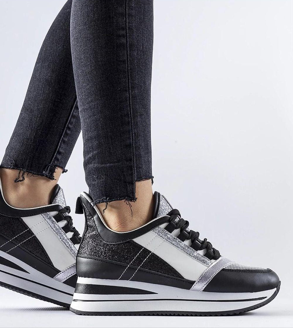 Black glitter Glevara platform sneakers on feet, showcasing elevated sole and lace-up design against a white background.