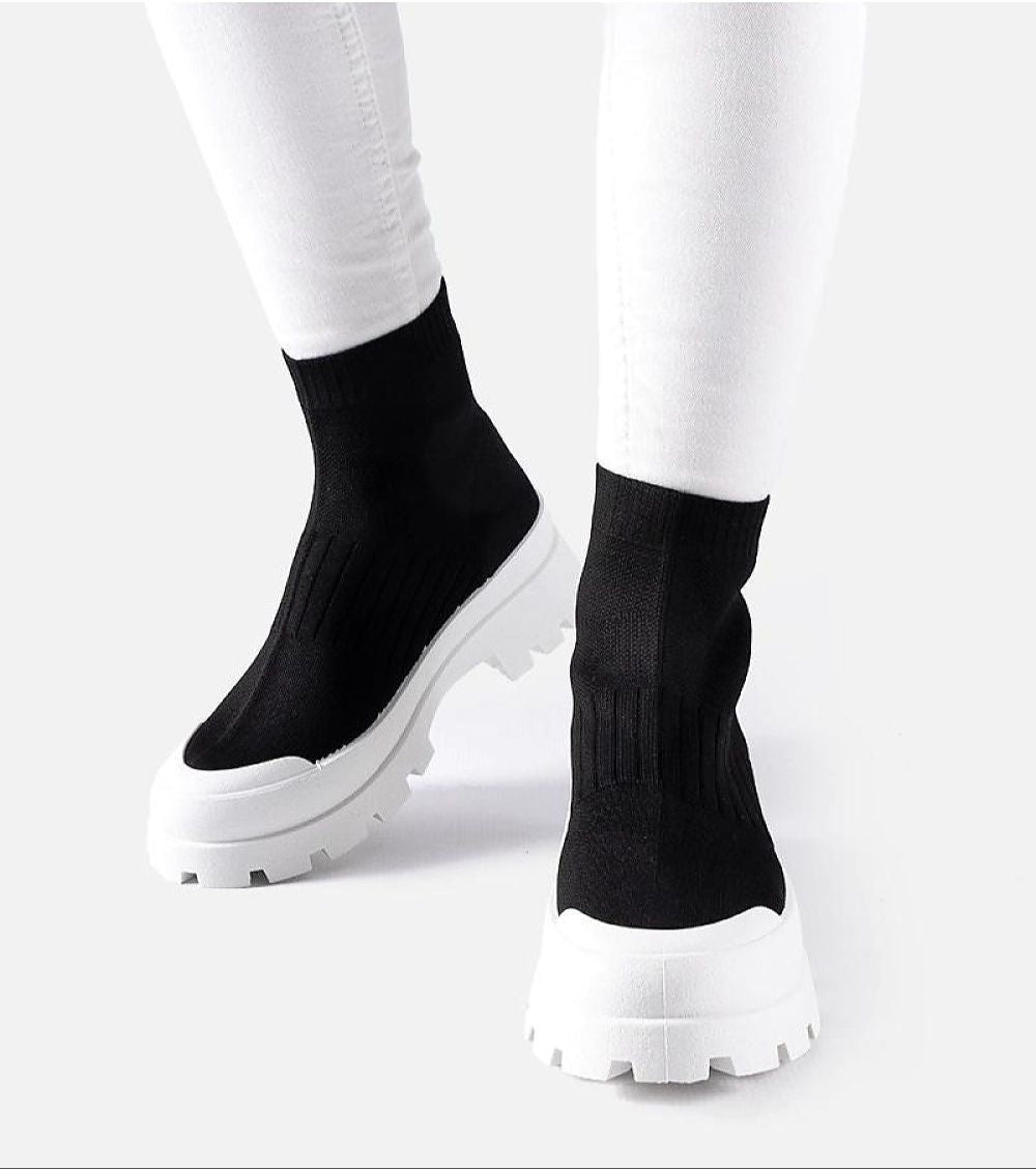 Velvone slip-on platform sneakers with black textile upper and white chunky sole, worn with white pants, ideal for spring fashion.