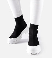 Velvone slip-on platform sneakers with black textile upper and white chunky sole, worn with white pants, ideal for spring fashion.
