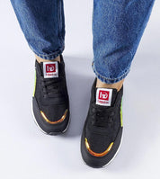 Person wearing black sneakers with metallic accents and denim jeans on a plain background.