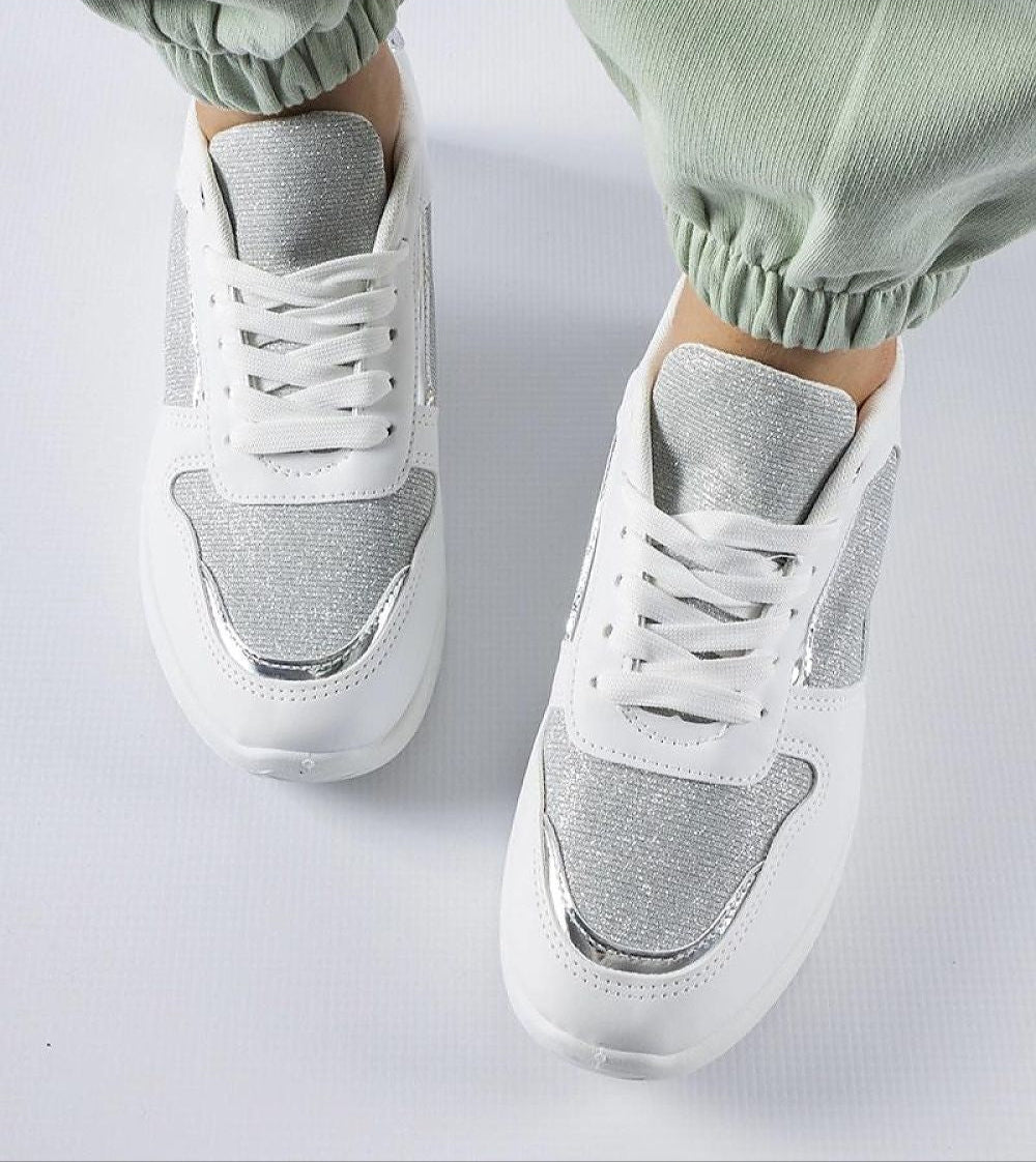 White lace-up women's sneakers with decorative stitching and breathable upper, paired with green joggers on a white background.